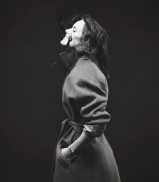 Black and white portrait of a woman in a belted coat with her head tilted back and hair blowing