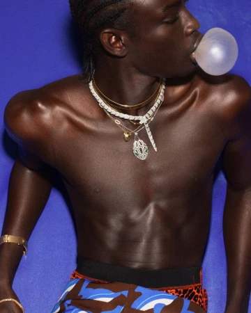 Man blowing bubble with bubblegum. Portrait of a fit, shirtless man with a deep skin tone against a bright blue backdrop.