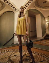 Model in yellow dress and tall boots holding a circular handle handbag inside a hotel lobby