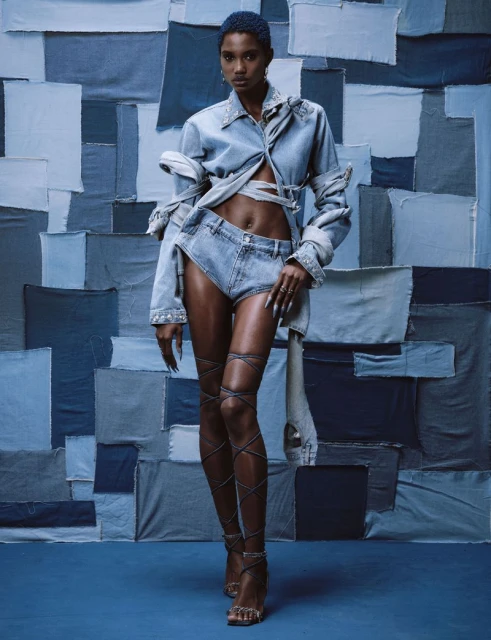 A solo model posing in a denim ensemble against a denim patchwork background, showcasing a distinctive fashion aesthetic with a full shot.