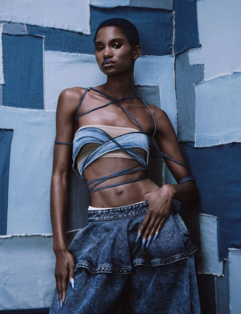 Fashionable black woman strikes a pose in a custom denim ensemble against a patchwork denim background in a studio shot.
