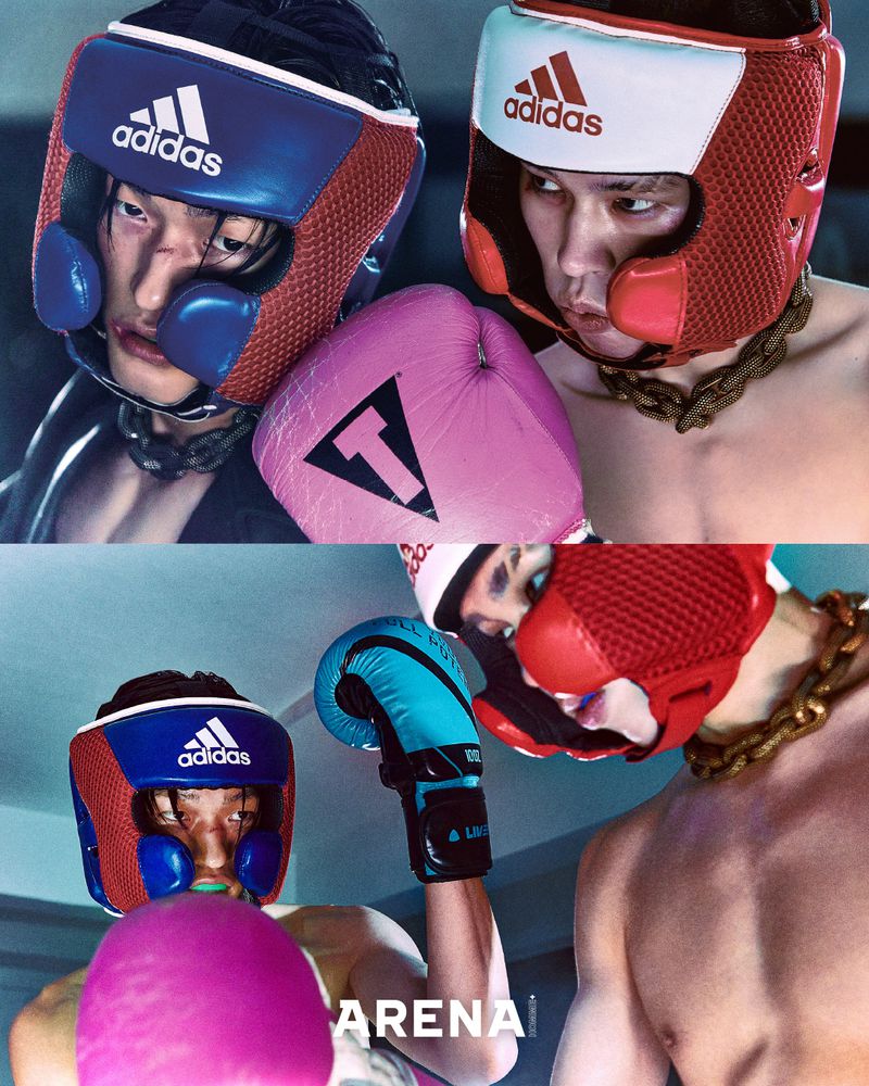 Two men wearing boxing headgear and gloves, facing each other with intense expressions in a dynamic composition with the Adidas logo visible.