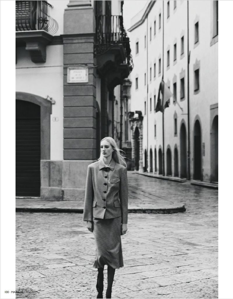 Model Ebba Bostrom walking on a cobblestone street in a skirt suit for Madame Germany, captured by Adriano Russo.