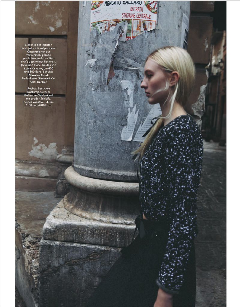 Profile view of a fair-skinned adult female in an outdoor urban fashion shot wearing a patterned top against an old building column.