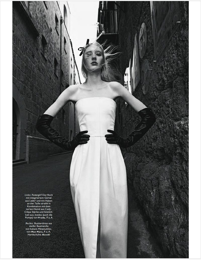 Model in white strapless dress and long black leather gloves posing in a narrow stone alleyway from a low angle
