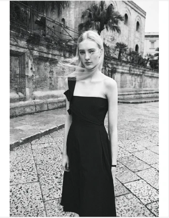 Monochrome outdoor portrait of a woman in a black dress on a cobblestone street with a vintage building and palm trees in the background.