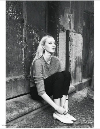 Black and white portrait of a blonde adult female sitting on a stone ledge with a textured wall in the background, looking upward.