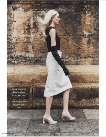 A blond woman models a black crop top, white skirt, and long gloves on a stone walkway, showcasing high-fashion style with a neutral backdrop.