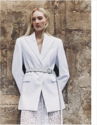 Model Ebba Bostrom wearing a structured white blazer belted at the waist against a rustic stone wall