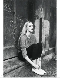Black and white editorial portrait of a model sitting on stone steps against a weathered doorway.