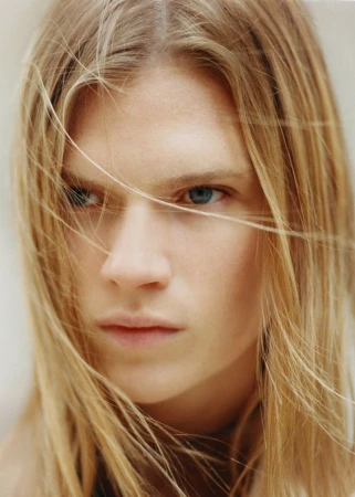 Close-up portrait of a blonde model with long hair blowing across her face for Puss Puss Magazine