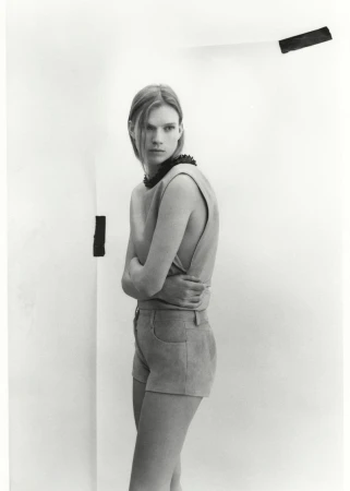 Black and white shot of a model in an open-backed top and shorts, arms crossed, standing against a graphic white wall.