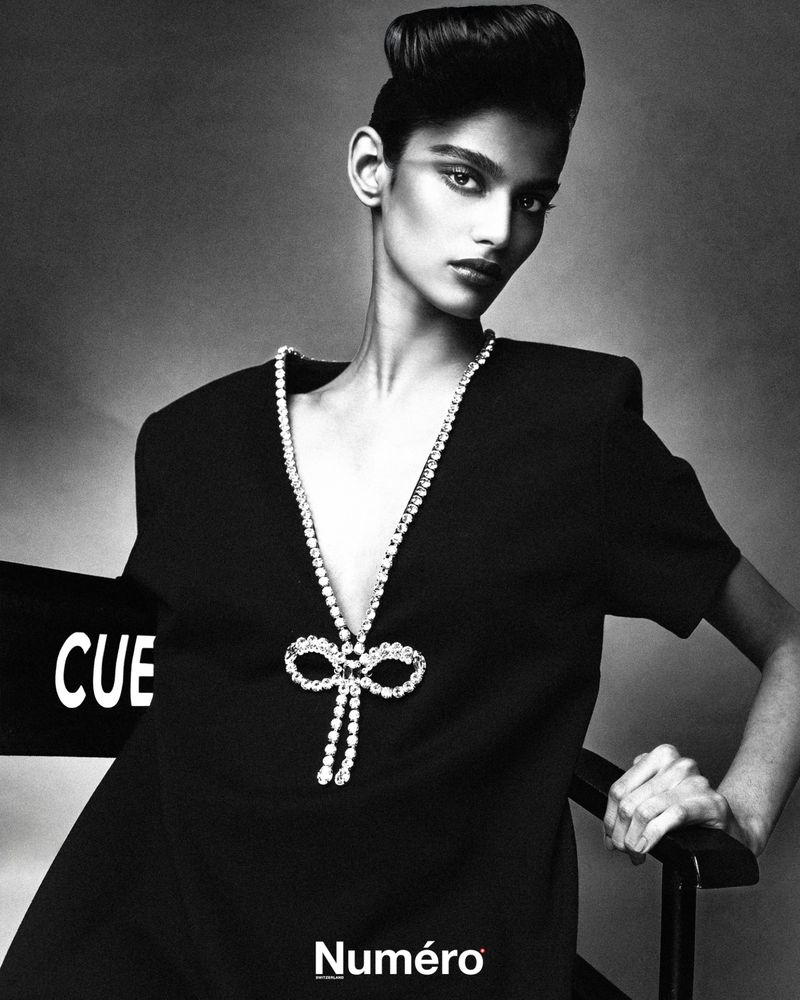A striking black and white fashion portrait of a young woman with a distinctive hairstyle, adorned with a sparkling necklace and couture dress.