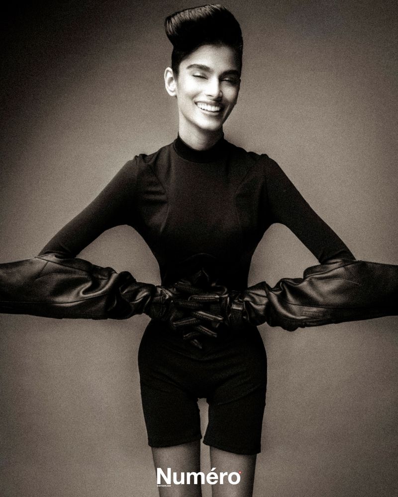 Model in a black top and shorts wearing long leather gloves against a grey studio backdrop for Numero Switzerland