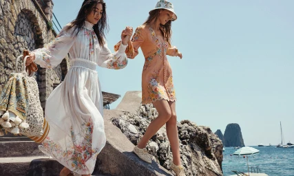 Two female models holding hands while walking down stone stairs by the ocean in Zimmermann resort wear fashion campaign.