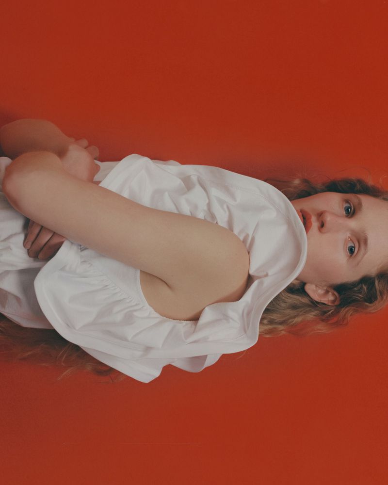 Model Eszter Vary wearing white ruffled top against solid red backdrop for Elle Greece