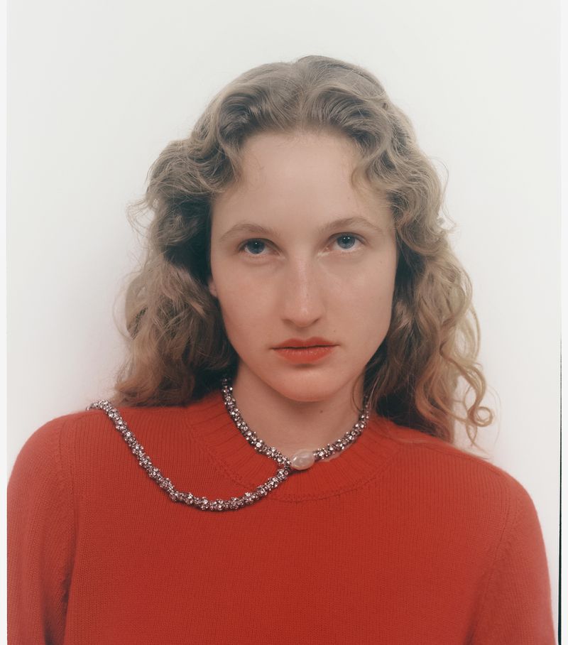 Model wearing a red top and crystal necklace against a plain background for Elle Greece