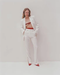 Model wearing a white pantsuit with red undergarments and red shoes standing against a neutral background