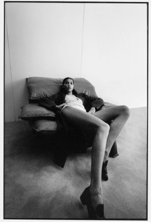 Elegant woman in repose on a chair wearing a robe and heels. The black-and-white portrait is set against a stark white wall.