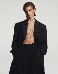 Model wearing an oversized black pinstripe blazer and layered gold necklaces against a neutral seamless background
