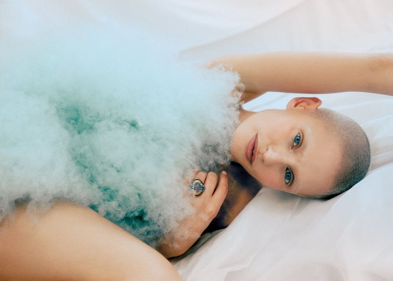 Model Bianca Balti reclining on white fabric draped in a light blue textured garment for Vanity Fair Italia, photographed by Noemi Ottilia Szabo.