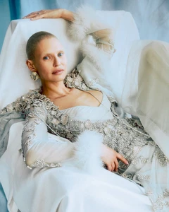 Model Bianca Balti reclining in a heavily embroidered gown with feathered cuffs against a pale backdrop for Vanity Fair Italia.