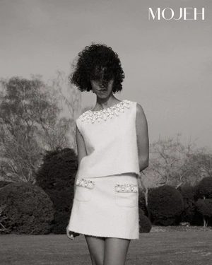Model with dark curly hair wearing an embellished white tweed skirt suit outdoors in a garden for Mojeh Magazine