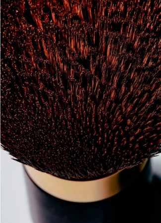 Closeup of a makeup brush with dark brown bristles, gold band, and dark handle, showcasing texture, detail, and color in a beauty context.