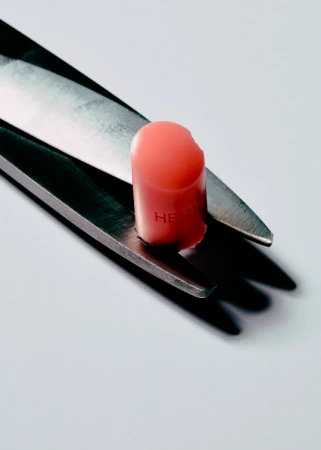 Close-up studio shot of peach-colored lipstick bullet held by the blades of a pair of stainless steel scissors on a white surface.