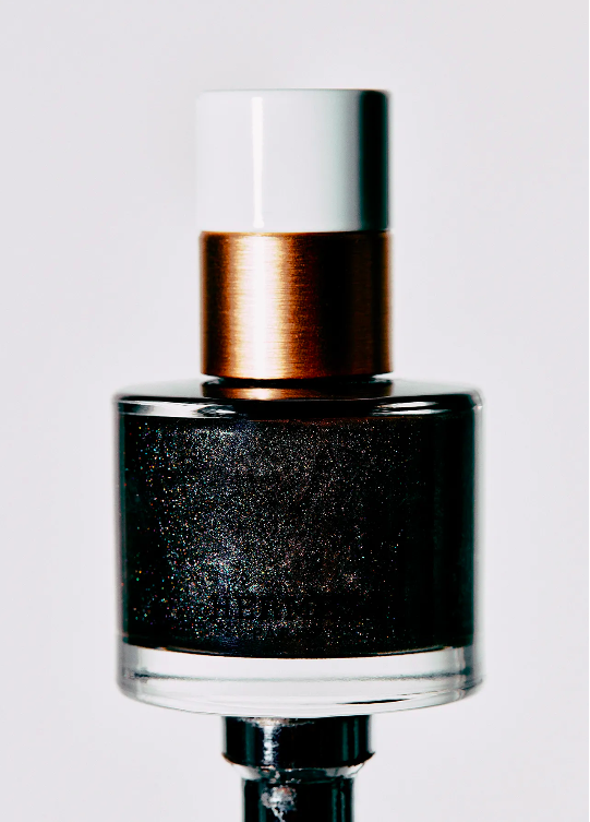 Macro shot of a bottle of dark sparkly nail polish with a white and copper cap, presented on a white background. Cosmetic photography.