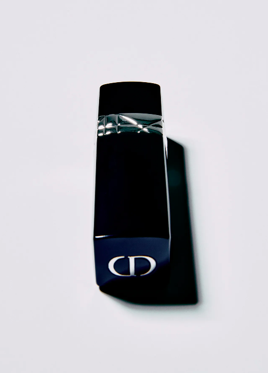 Close-up studio shot of a black Dior fragrance bottle with silver accents against a bright white backdrop. Shadow is visible.