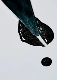 Close-up of a metal spatula slicing through a glossy black gel smear on a plain white surface with a small droplet below.
