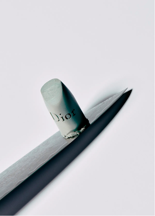 Close-up still life shot of a Dior lip pencil with a gray lead, placed on a sharpener, against a bright, white backdrop in a studio.