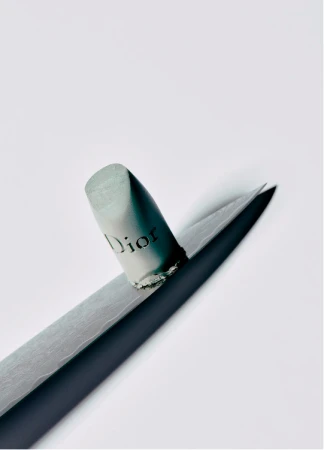 Close-up still life shot of a Dior lip pencil with a gray lead, placed on a sharpener, against a bright, white backdrop in a studio.