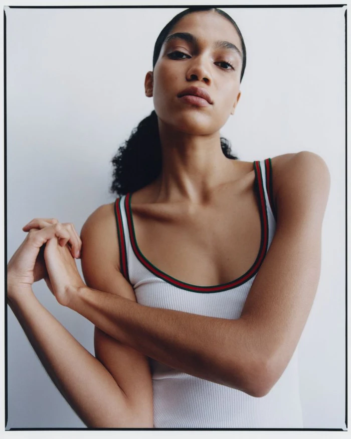 Model Raynara Negrine wearing a white tank top with green and red striped trim against a light background