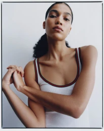 Model Raynara Negrine wearing a white tank top with green and red striped trim against a light background