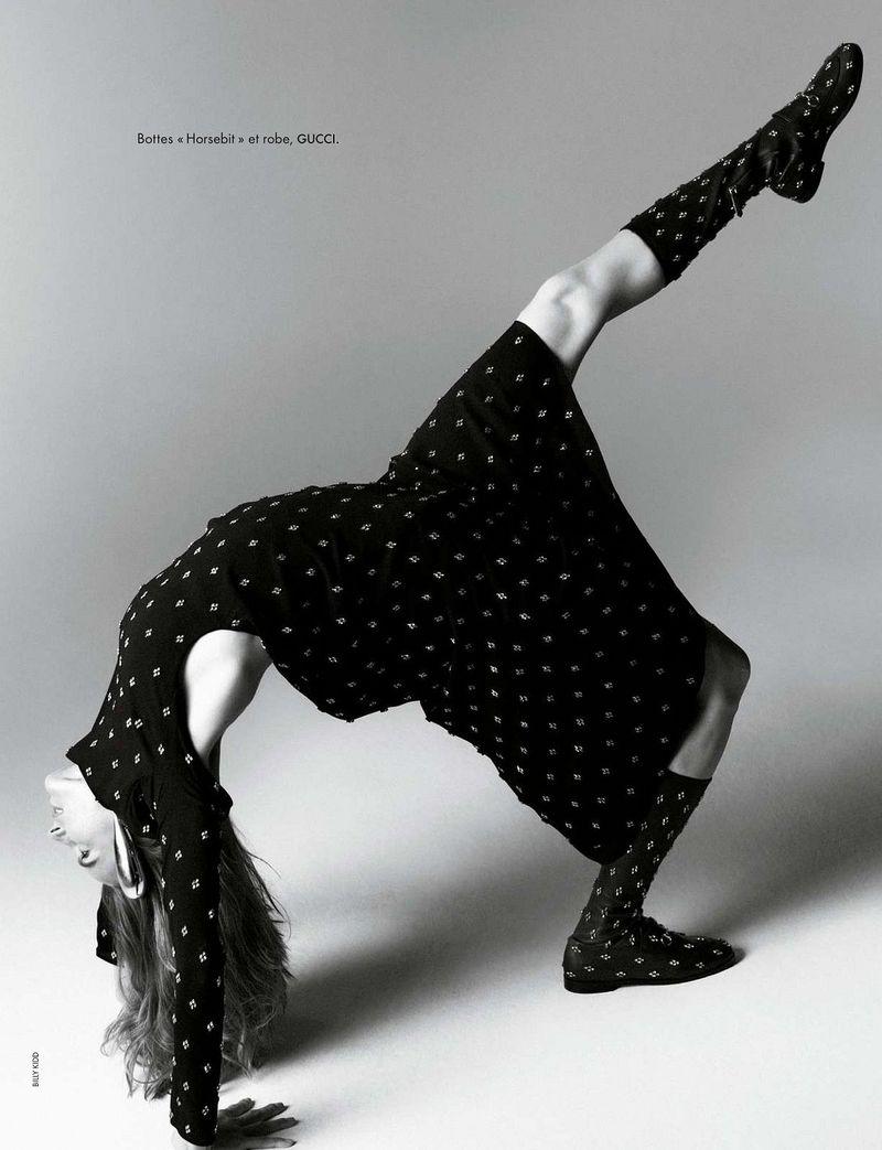 Model in a black patterned dress bending backward in a dramatic arch against a plain grey studio background.