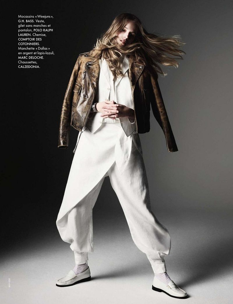 Fashion editorial shot of a model wearing an off-white linen suit and brown leather motorcycle jacket in a graded studio setting.