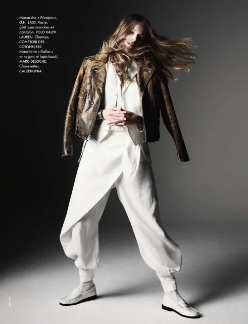 Fashion editorial shot of a model wearing an off-white linen suit and brown leather motorcycle jacket in a graded studio setting.