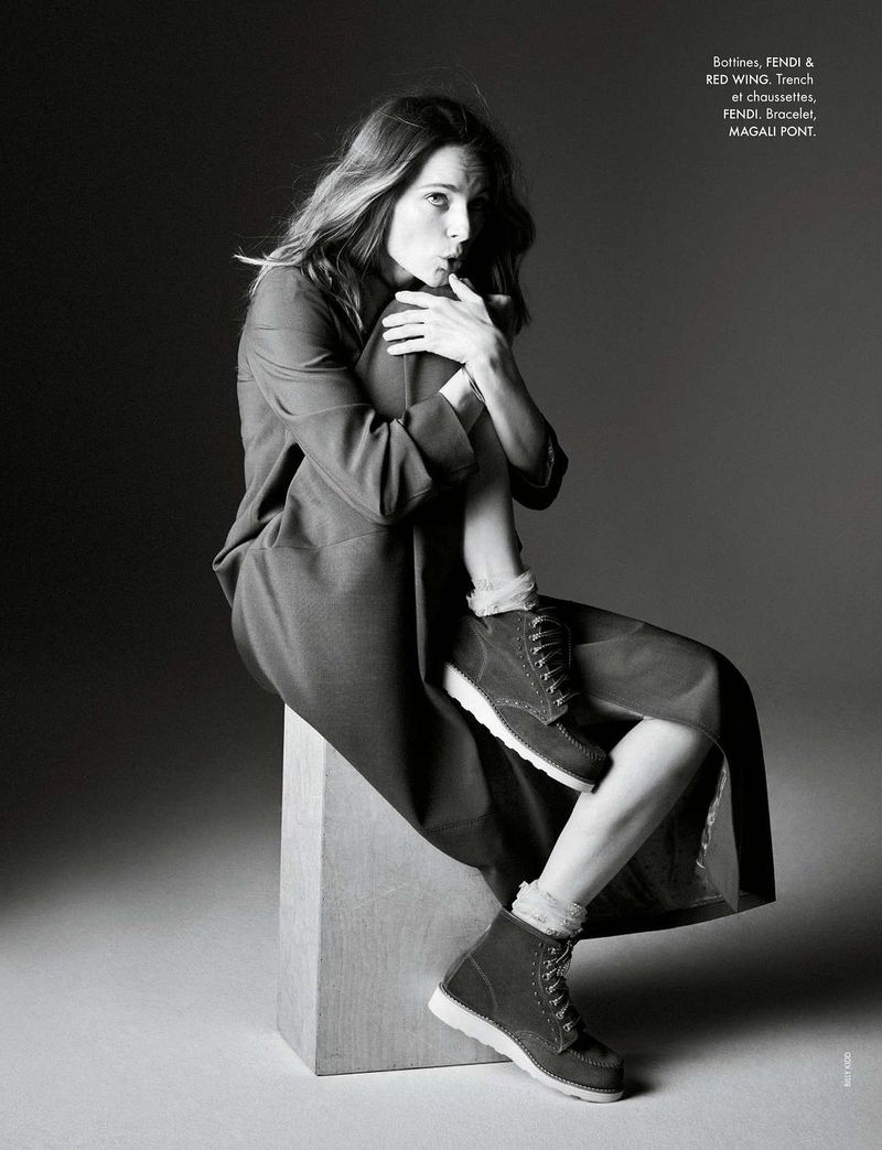 Black and white portrait of a woman in a jacket and boots, sitting on a block, posing in a photo studio, fashion editorial shot.