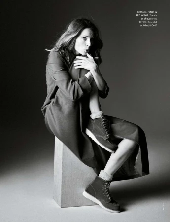 Black and white portrait of a woman in a jacket and boots, sitting on a block, posing in a photo studio, fashion editorial shot.