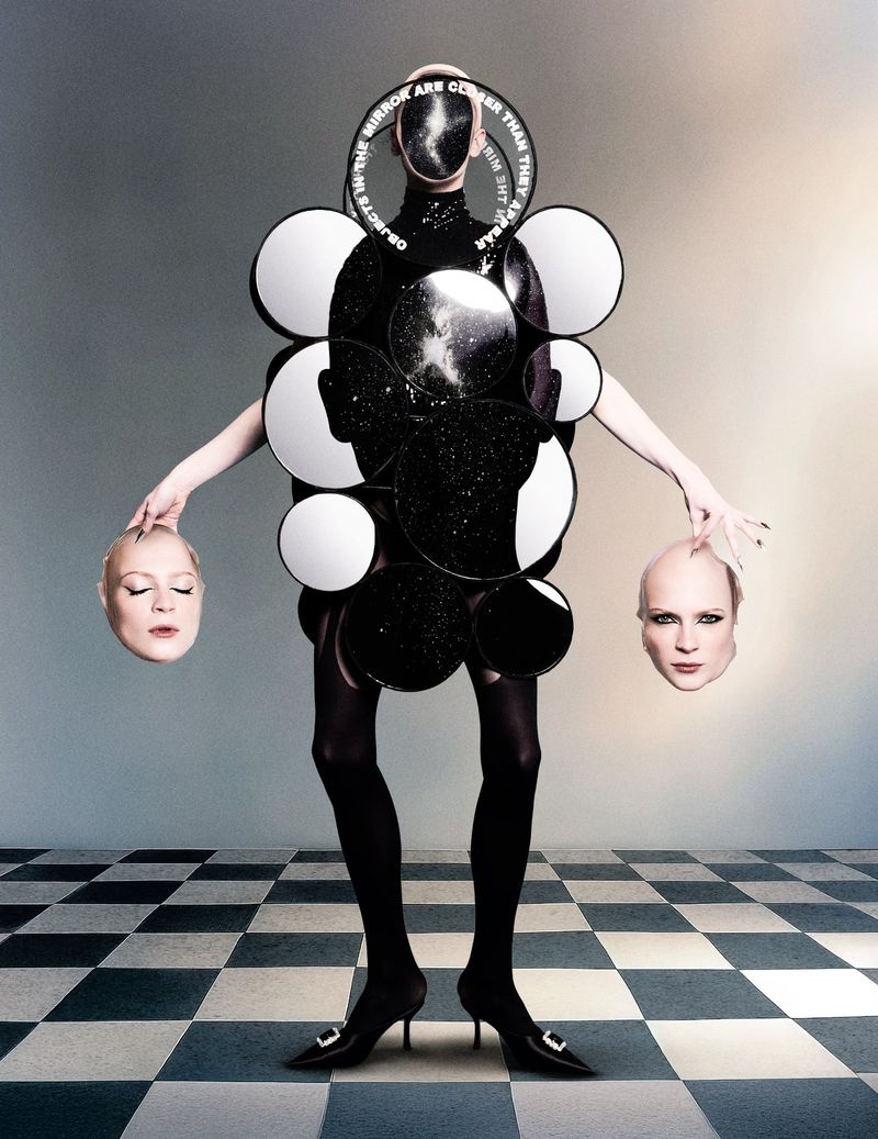 Avant-garde fashion shot featuring a person in a mirror-decorated garment holding two mannequin heads on a checkered floor.
