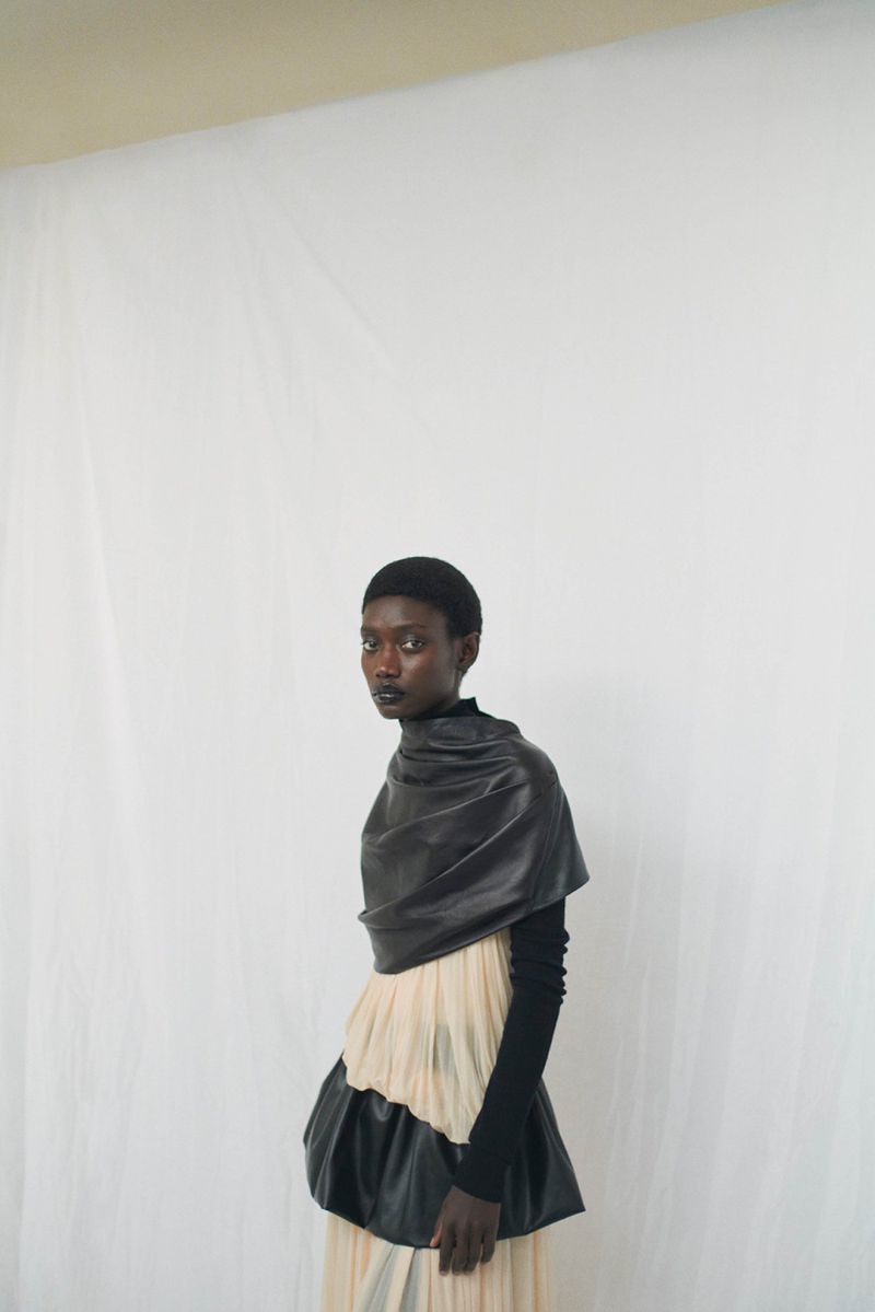 Elegant Black woman in a black top and layered skirt against a white backdrop in a studio fashion portrait with soft, diffused lighting.