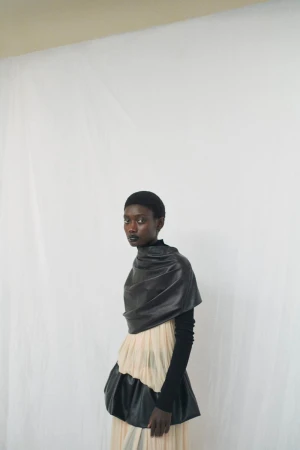 Elegant Black woman in a black top and layered skirt against a white backdrop in a studio fashion portrait with soft, diffused lighting.