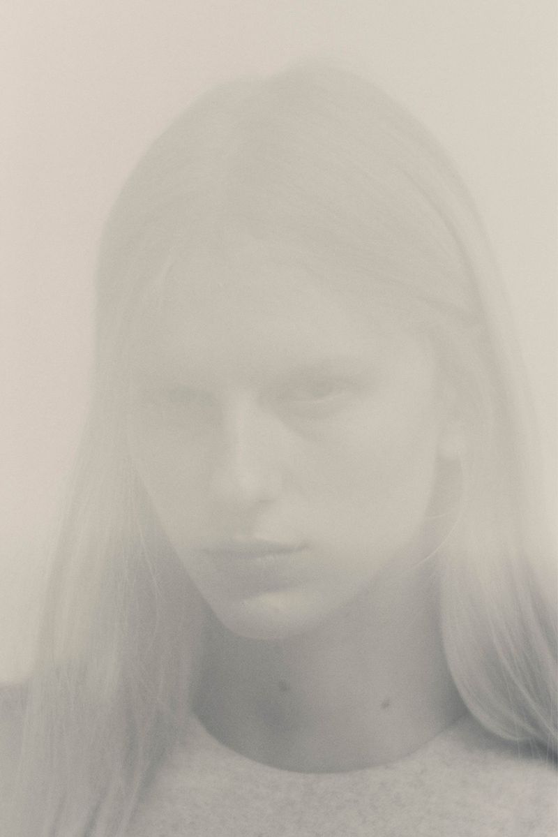 Close-up portrait of a model with long hair against a light neutral background captured with a soft double exposure effect.