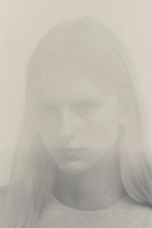 Close-up portrait of a model with long hair against a light neutral background captured with a soft double exposure effect.