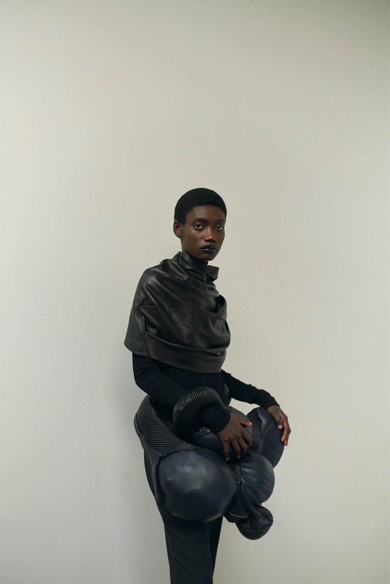 Fashionable short-haired Black female model poses in a photo studio wearing a black outfit with avant-garde, bubble-style accents.