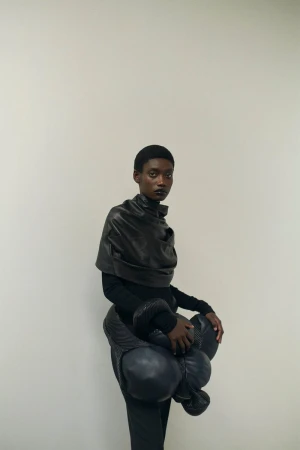 Fashionable short-haired Black female model poses in a photo studio wearing a black outfit with avant-garde, bubble-style accents.