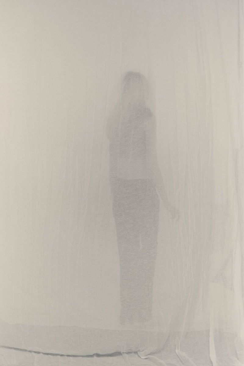 Abstract figure of a woman in an ethereal, dreamlike setting created by soft diffused lighting and sheer white fabric backdrop.