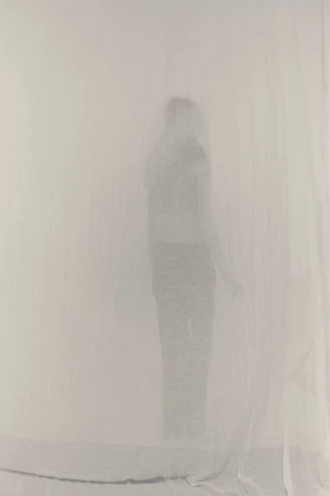Abstract figure of a woman in an ethereal, dreamlike setting created by soft diffused lighting and sheer white fabric backdrop.